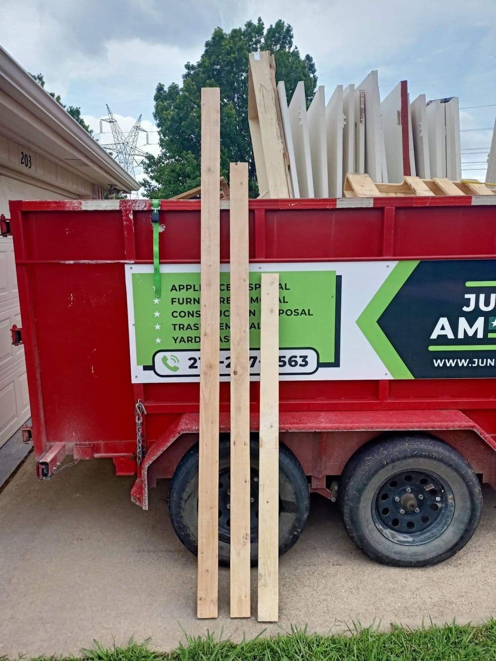 Wooden planks leaning against a red dumpster for furniture disposal and recycling.