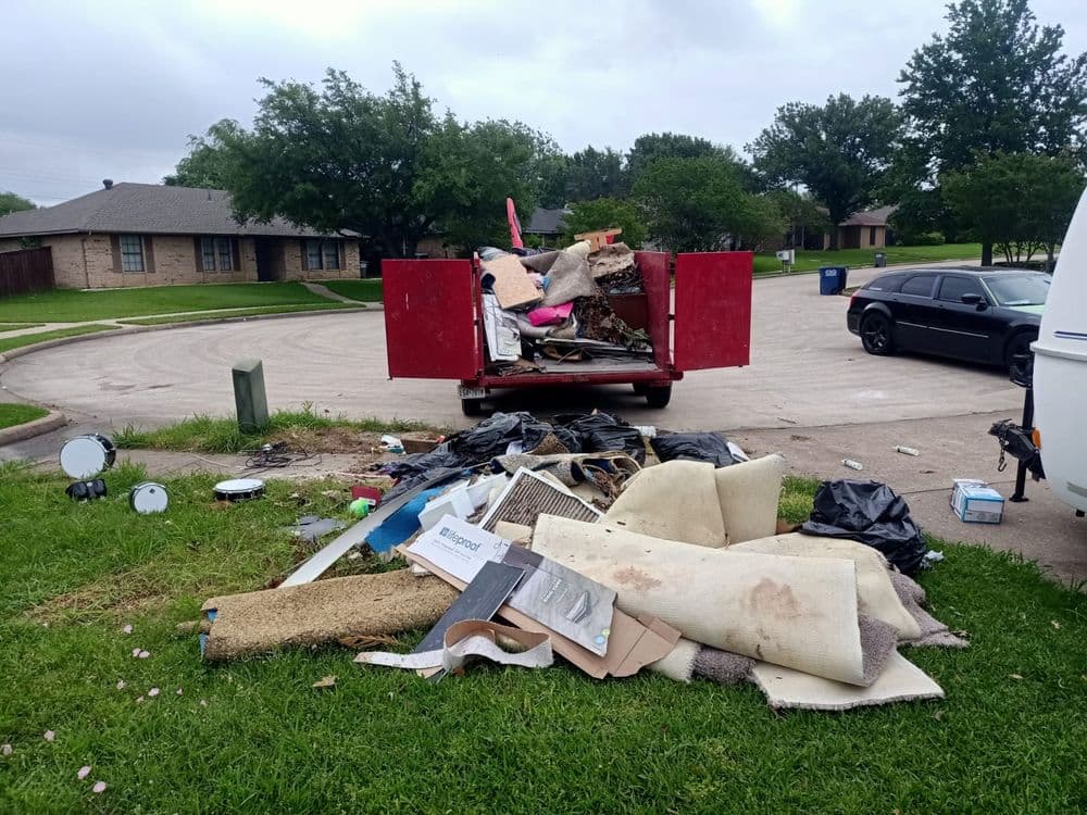 Overflowing dumpster with debris on grass, including furniture and construction materials.