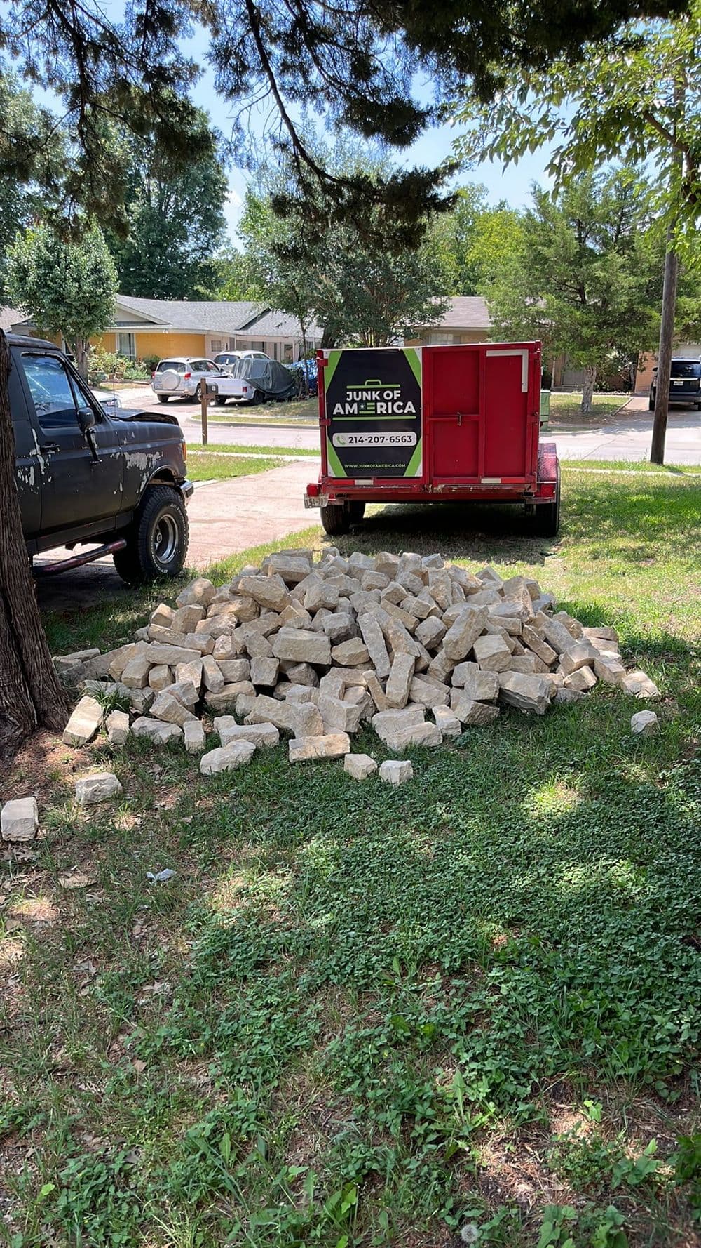 Pile of rocks near a junk removal trailer in a residential area with trees.
