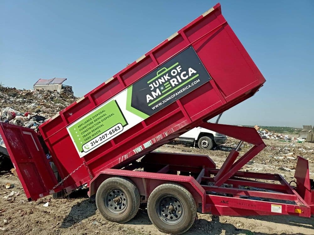 Red junk removal dumpster from Junk of America at a landfill site with contact information visible.