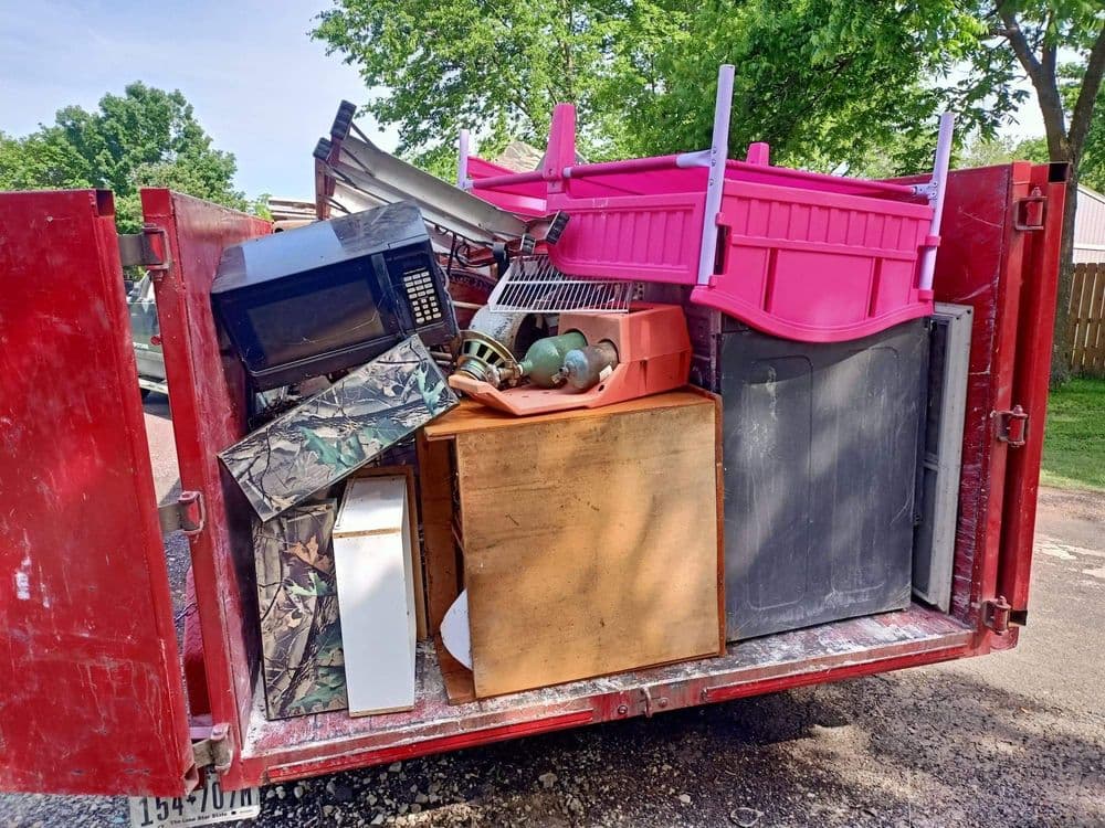 Red dumpster filled with assorted furniture, appliances, and colorful storage containers.