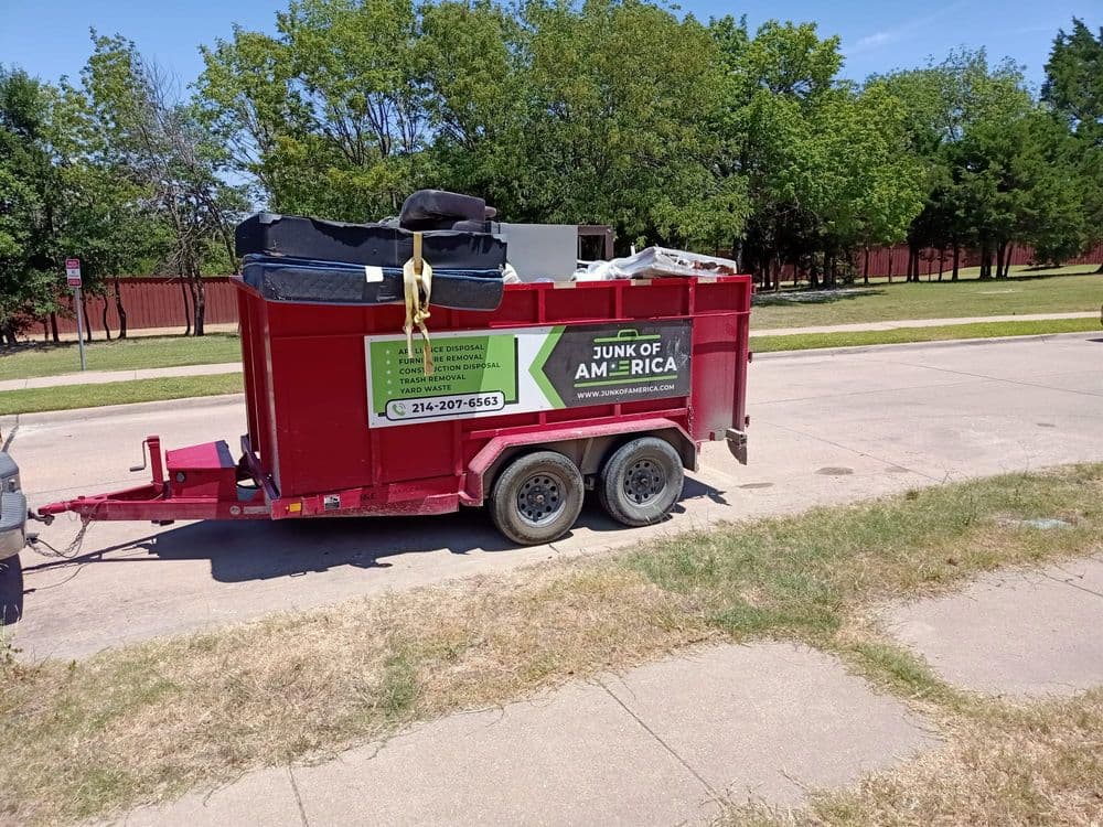 Red junk removal trailer parked on a residential street with furniture and debris inside.