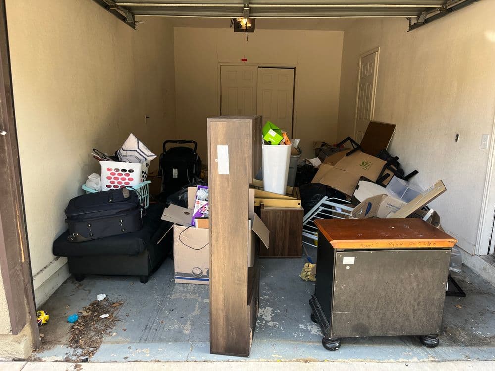Cluttered garage filled with boxes, furniture, and various items ready for organization or disposal.