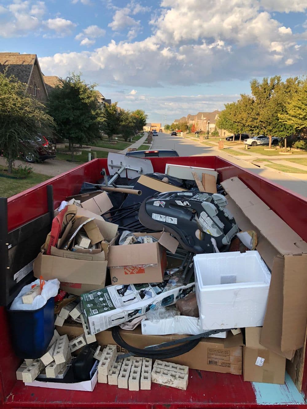 Full dumpster filled with cardboard boxes and discarded household items on a suburban street.