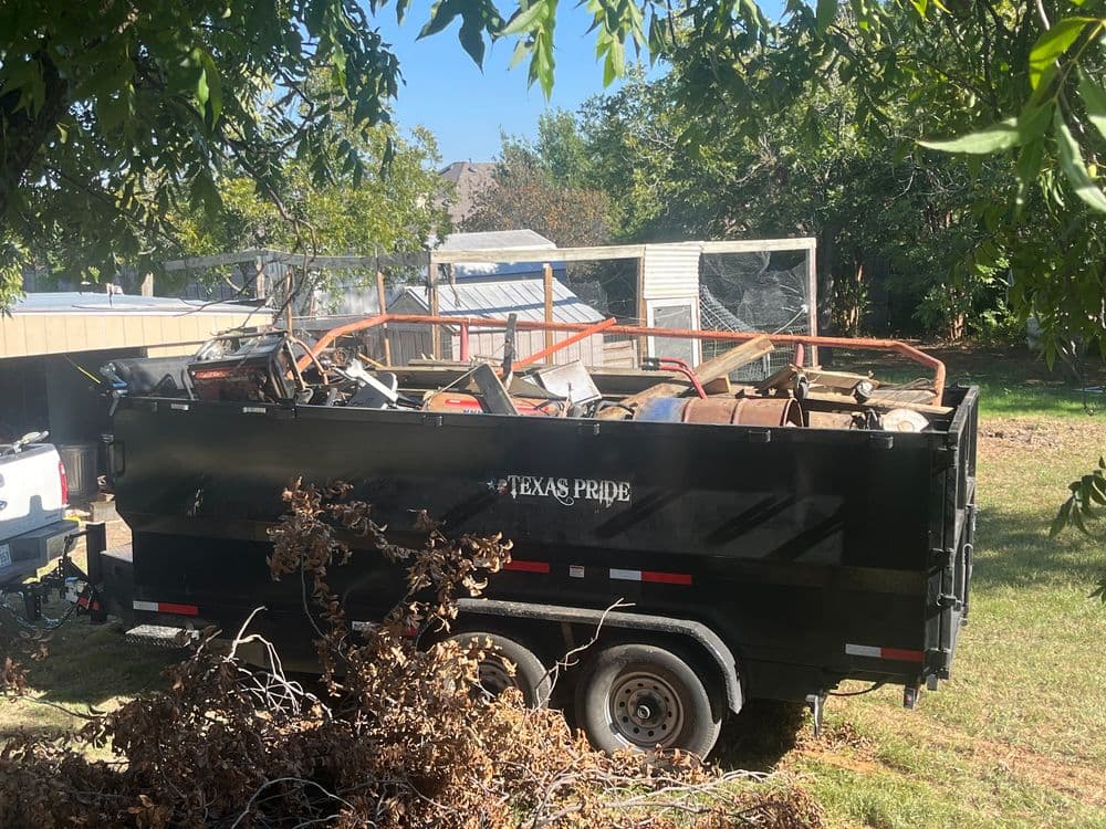 Texas Pride dump trailer filled with debris and construction materials in a yard setting.
