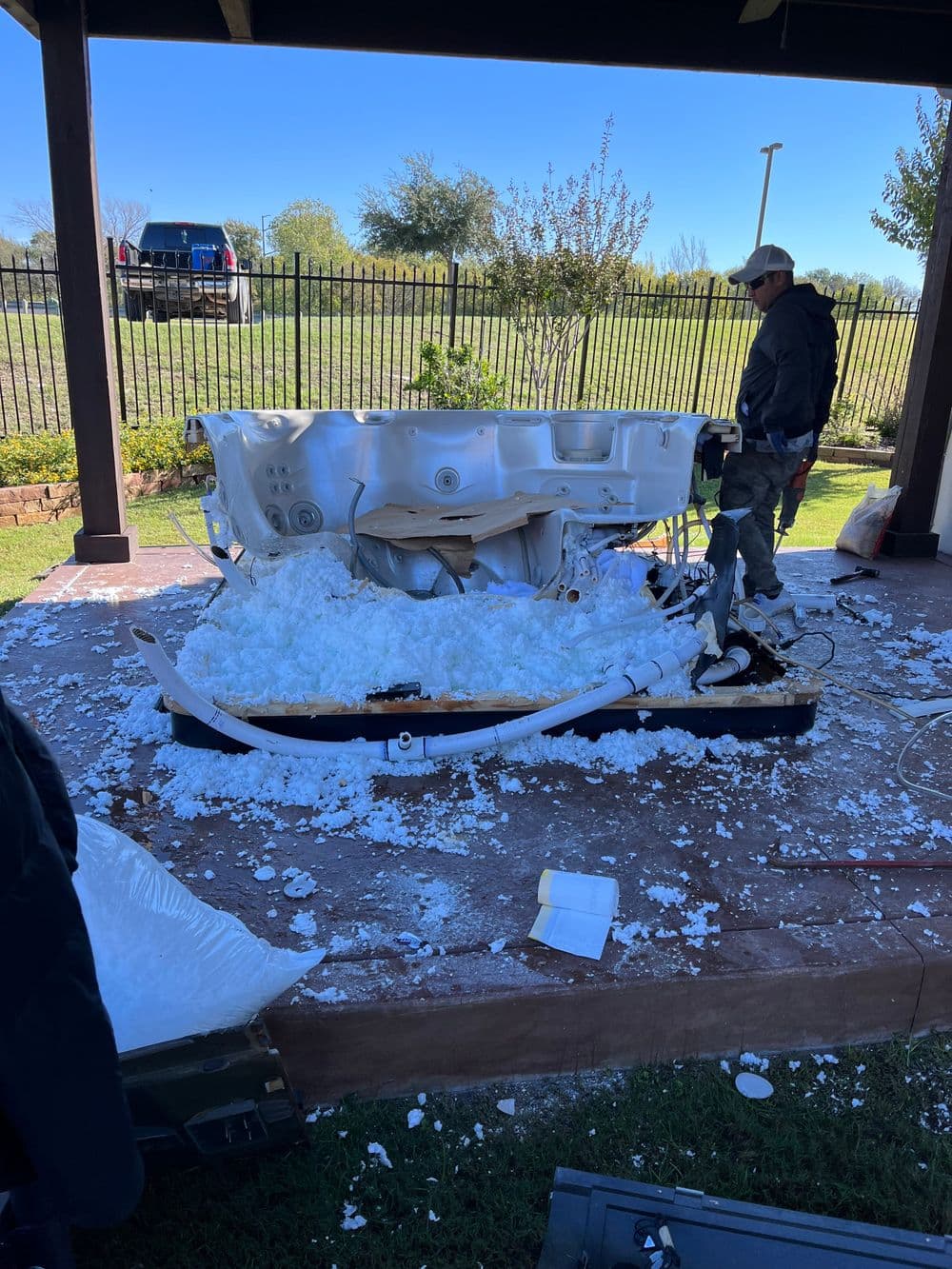 Hot tub repair in progress with foam insulation scattered on the ground and a technician working.