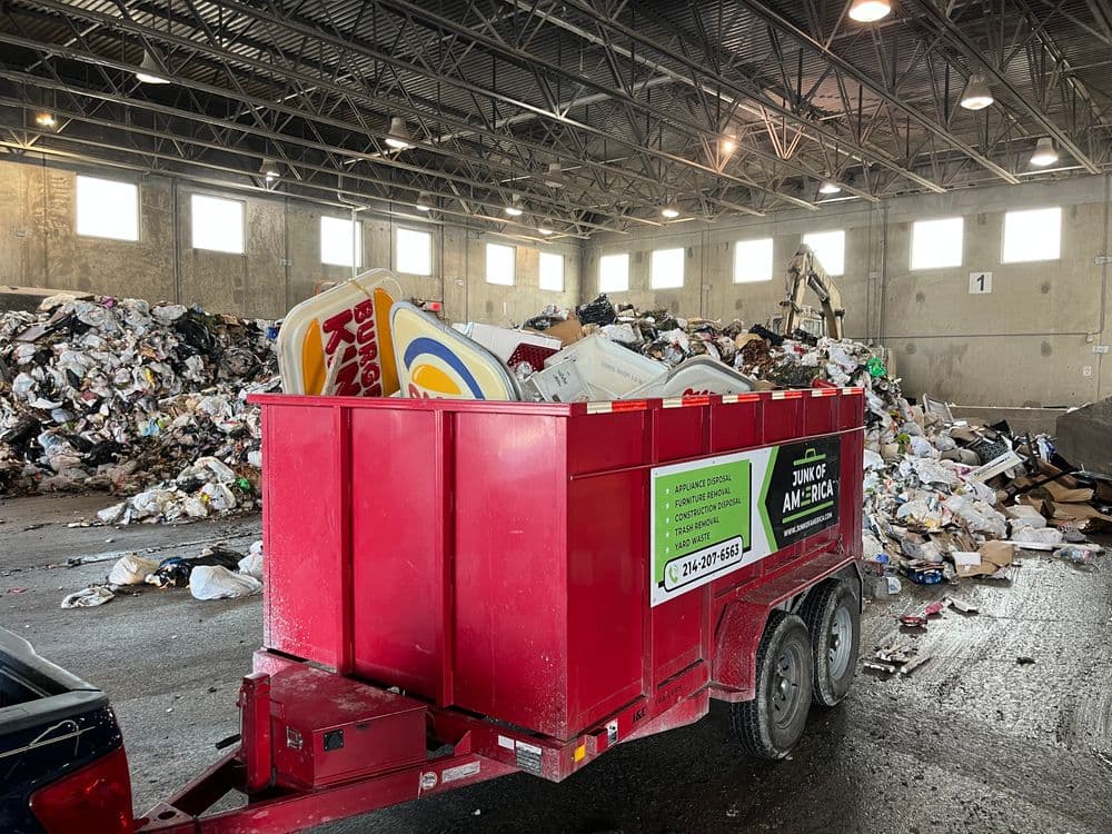Red junk removal trailer in a recycling center filled with waste and debris.