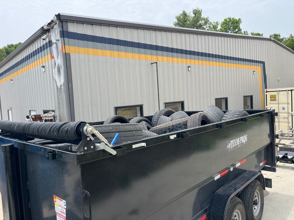 Dump trailer filled with old tires parked near a warehouse building.