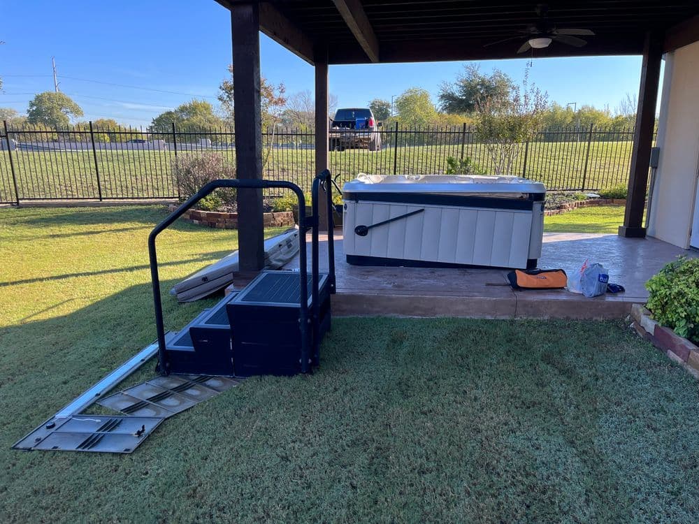 Hot tub installation with ramp and steps in a backyard setting on a sunny day.