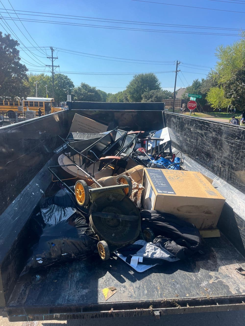 Dump truck filled with discarded furniture, boxes, and debris on a sunny day.