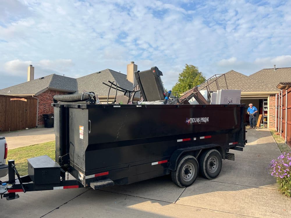 Black dumpster filled with furniture and debris, parked in a residential driveway.