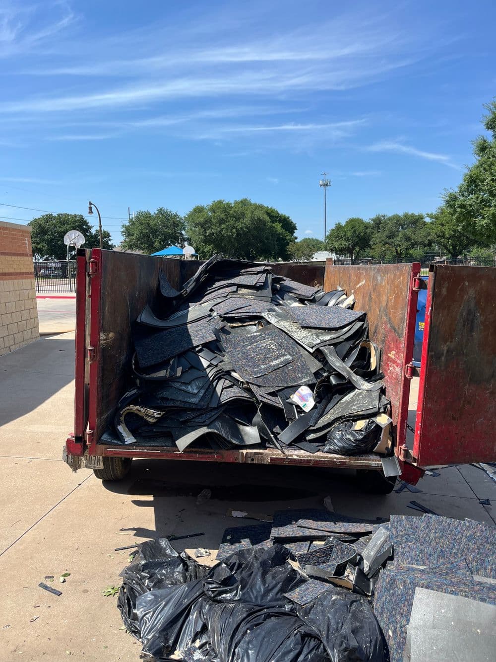 Dump truck filled with shredded rubber flooring and debris under a clear blue sky.
