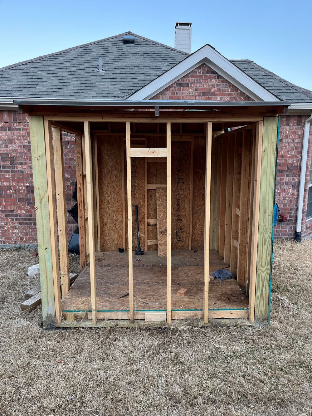 Under-construction wooden shed with exposed framing and a grassy backyard.