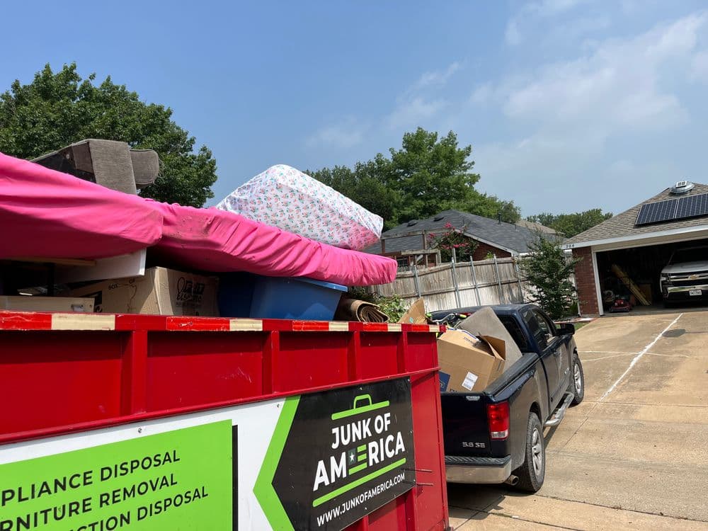 Red dumpster filled with junk, including a mattress and boxes, in a residential area.