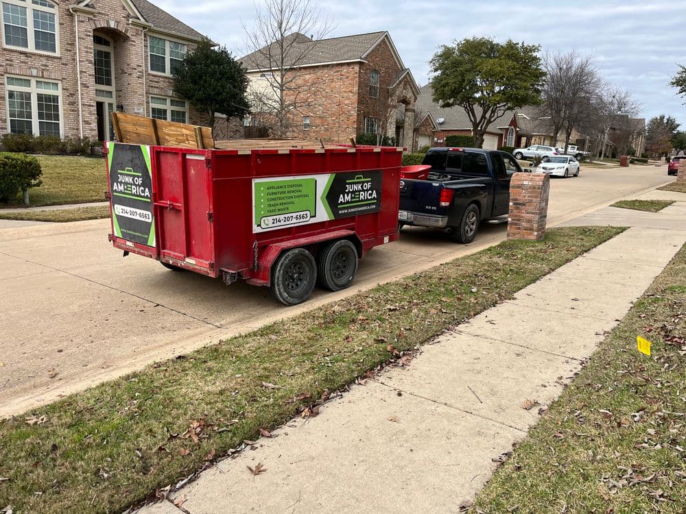 Red junk removal trailer parked on residential street next to a pickup truck.